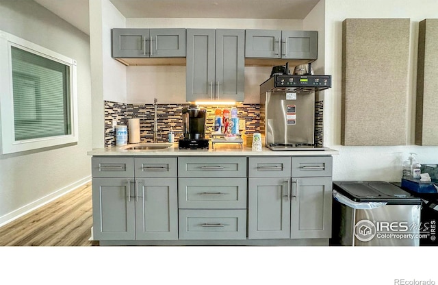 kitchen featuring light countertops, decorative backsplash, gray cabinets, light wood-style floors, and a sink