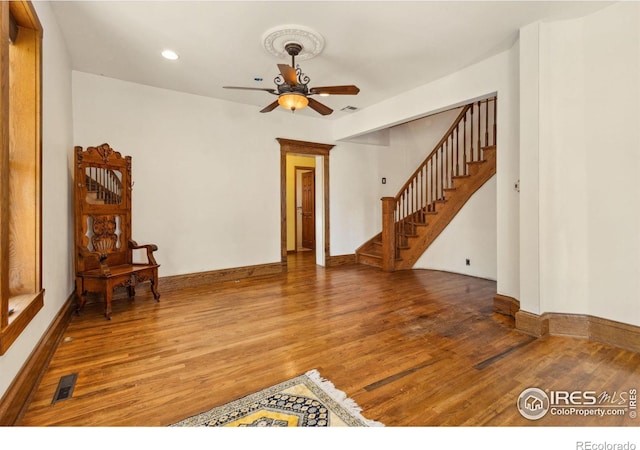 living area with stairway, wood finished floors, visible vents, and ceiling fan