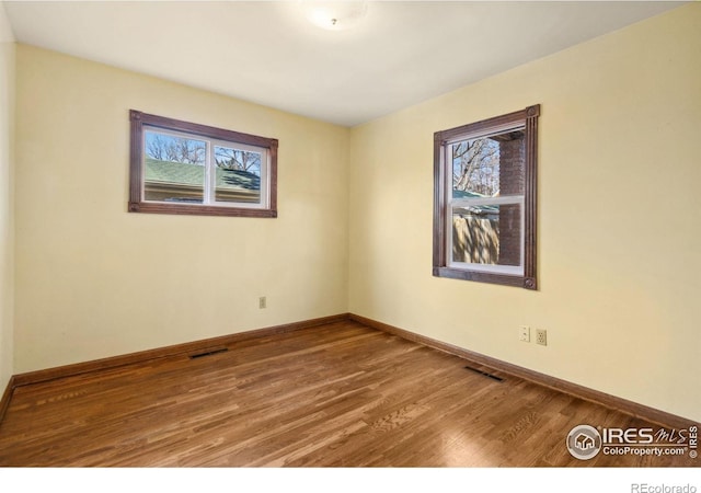 spare room with plenty of natural light, wood finished floors, and visible vents