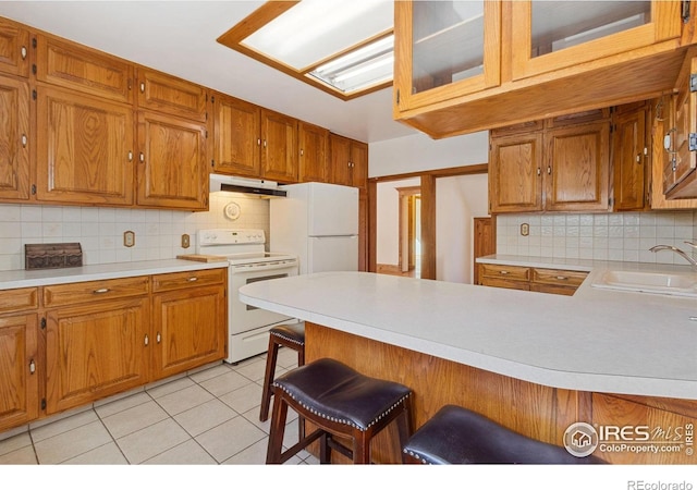 kitchen featuring white appliances, light tile patterned floors, a sink, light countertops, and under cabinet range hood