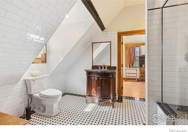 bathroom with tile patterned flooring, toilet, vanity, vaulted ceiling, and tile walls