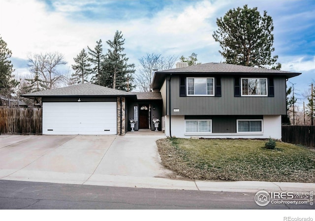 tri-level home featuring an attached garage, driveway, a front yard, and fence