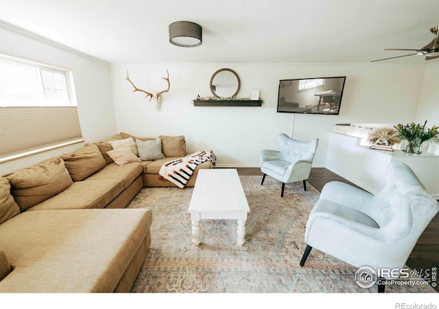 living area with crown molding, wood finished floors, baseboards, and ceiling fan