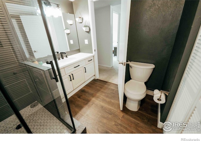 bathroom with toilet, a stall shower, wood finished floors, baseboards, and vanity