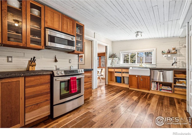 kitchen featuring dark wood-style flooring, a sink, stainless steel appliances, dark countertops, and brown cabinets