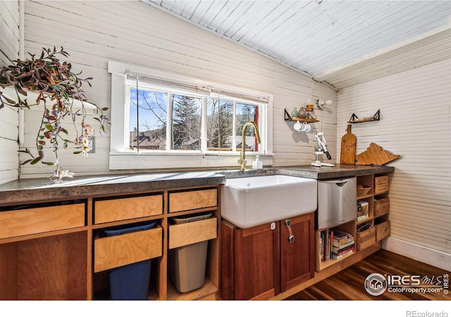 kitchen with brown cabinetry, a sink, vaulted ceiling, dark wood-type flooring, and dark countertops