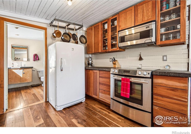 kitchen featuring dark wood-type flooring, glass insert cabinets, appliances with stainless steel finishes, dark countertops, and brown cabinets