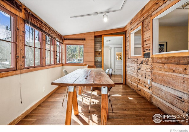 dining area featuring wooden walls, baseboards, vaulted ceiling, track lighting, and wood-type flooring