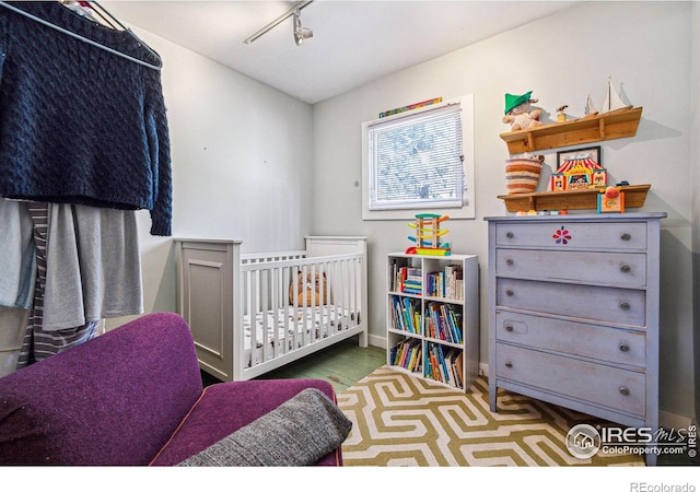 bedroom featuring track lighting, a nursery area, wood finished floors, and baseboards