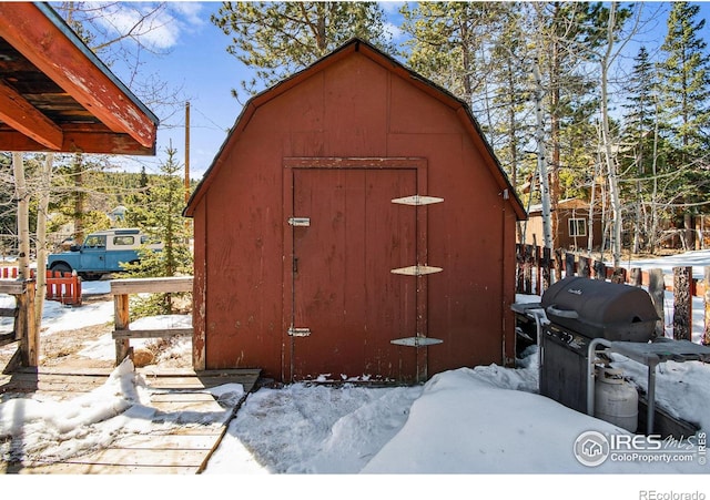 snow covered structure featuring an outbuilding and a shed