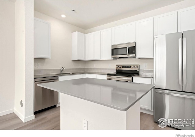 kitchen with light wood finished floors, a kitchen island, a sink, stainless steel appliances, and white cabinets