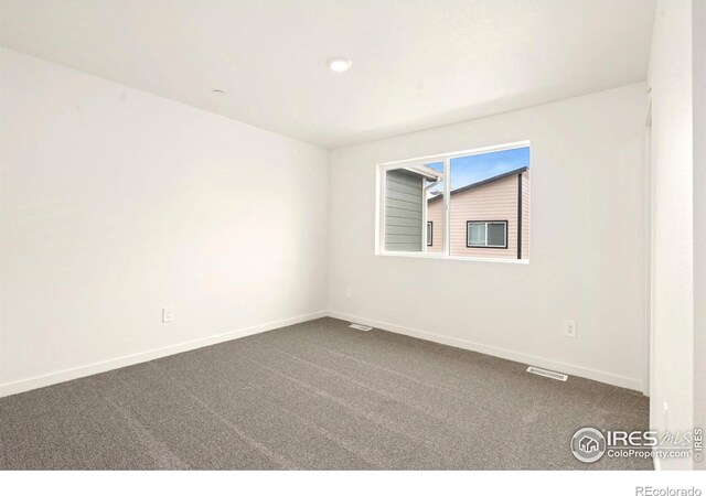 spare room with visible vents, baseboards, and dark carpet