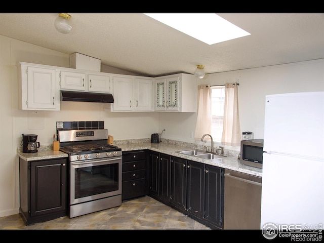 kitchen featuring a sink, under cabinet range hood, appliances with stainless steel finishes, white cabinets, and dark cabinets