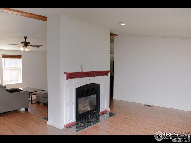 living area featuring ceiling fan, visible vents, a fireplace with flush hearth, and wood finished floors