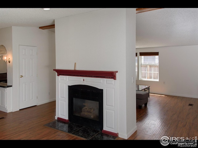 living room featuring lofted ceiling with beams, a textured ceiling, a glass covered fireplace, dark wood-style floors, and baseboards