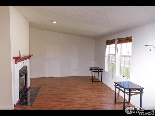 living room featuring a fireplace with flush hearth, wood finished floors, visible vents, and a textured ceiling