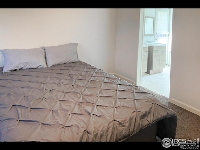 bedroom with a sink, baseboards, light colored carpet, and ensuite bath