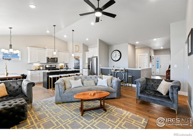 living area featuring wood finished floors, baseboards, high vaulted ceiling, recessed lighting, and ceiling fan with notable chandelier