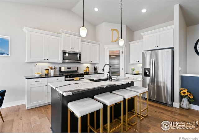 kitchen with an island with sink, wood finished floors, white cabinetry, stainless steel appliances, and a breakfast bar area