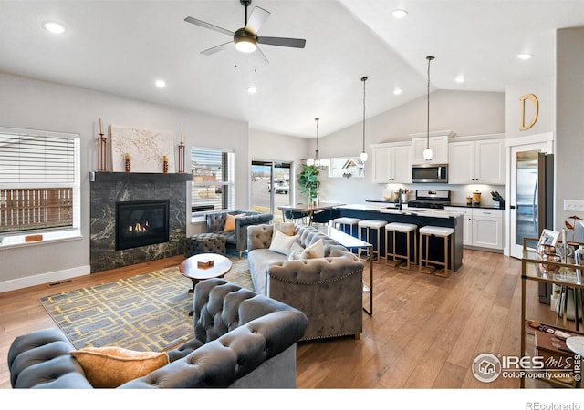 living room with a high end fireplace, ceiling fan, light wood-type flooring, recessed lighting, and high vaulted ceiling