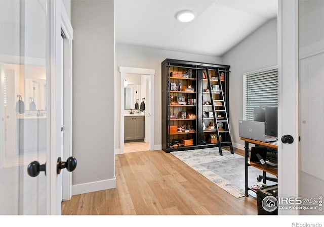 home office with a sink, baseboards, lofted ceiling, and wood finished floors