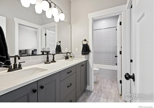 bathroom featuring double vanity, backsplash, toilet, and a sink