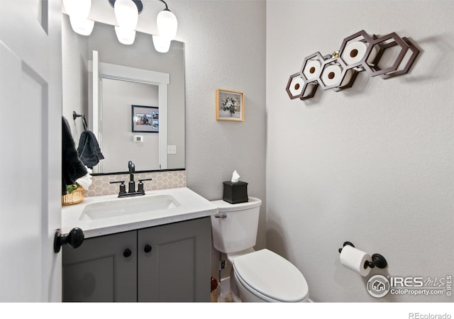 half bath with backsplash, vanity, and toilet