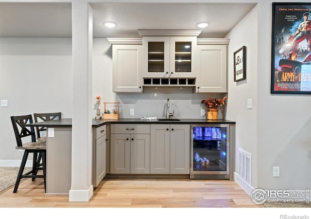 bar with beverage cooler, baseboards, light wood-style flooring, a sink, and indoor wet bar