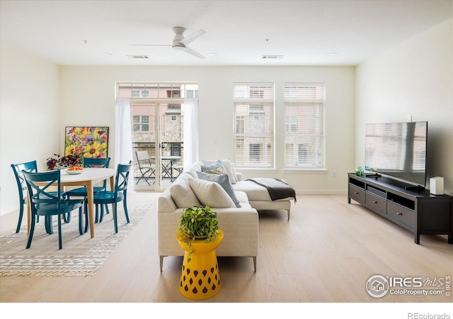 living room with visible vents, light wood-style flooring, baseboards, and ceiling fan