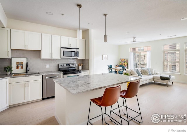 kitchen featuring a sink, light wood-style floors, appliances with stainless steel finishes, a breakfast bar area, and decorative backsplash