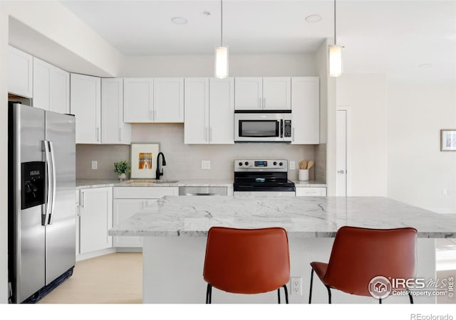 kitchen with tasteful backsplash, a kitchen breakfast bar, white cabinets, stainless steel appliances, and a sink