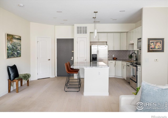 kitchen featuring light wood finished floors, visible vents, backsplash, a kitchen island, and appliances with stainless steel finishes