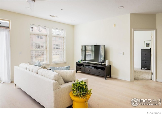 living area with light wood-type flooring, visible vents, and baseboards