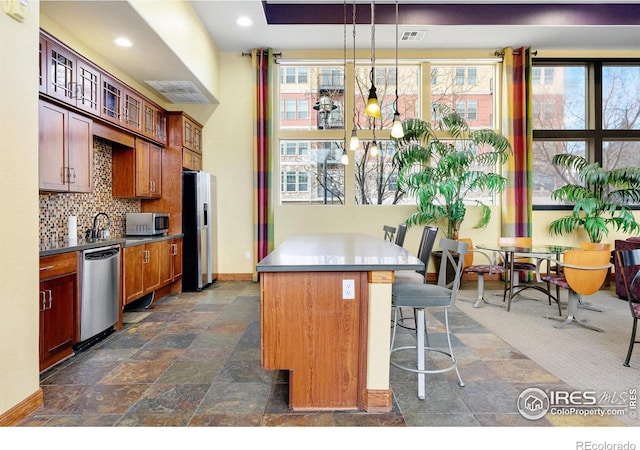 kitchen featuring a kitchen island, stone finish flooring, a breakfast bar area, decorative backsplash, and appliances with stainless steel finishes