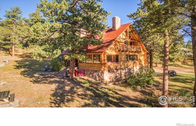 view of front of house featuring log siding, a chimney, and roof with shingles