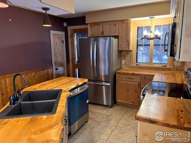 kitchen featuring a sink, butcher block countertops, appliances with stainless steel finishes, decorative light fixtures, and a chandelier