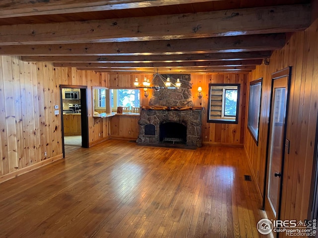 unfurnished living room featuring visible vents, beam ceiling, hardwood / wood-style floors, wooden walls, and a fireplace