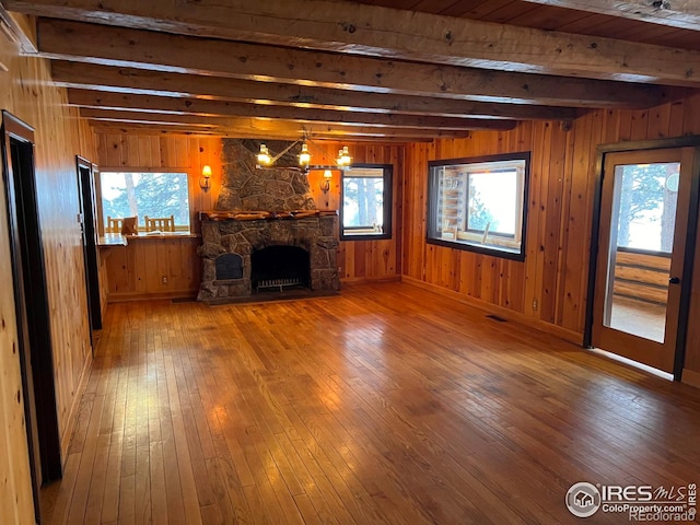 unfurnished living room with a stone fireplace, hardwood / wood-style flooring, beamed ceiling, and a healthy amount of sunlight