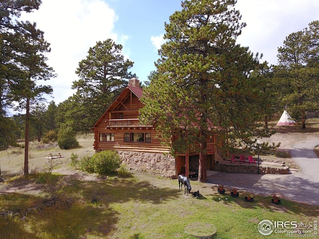 view of front of property featuring log exterior, an attached garage, a chimney, and a front yard