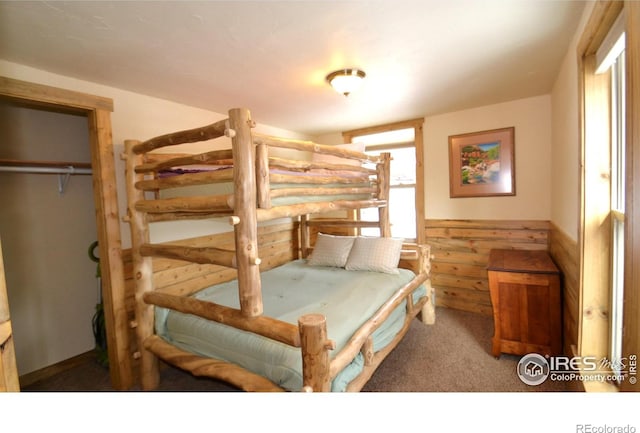 bedroom featuring a closet, wainscoting, carpet flooring, and wood walls