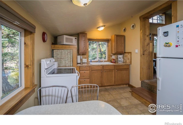 kitchen with brown cabinetry, white appliances, lofted ceiling, and a sink