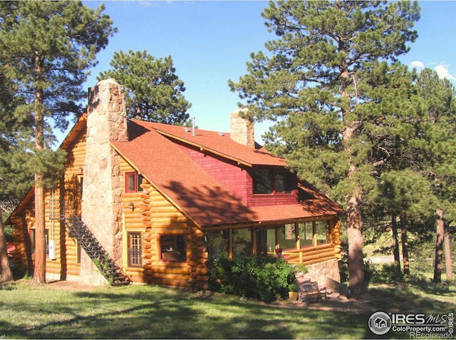 log cabin featuring stairway, a front yard, a shingled roof, log exterior, and a chimney