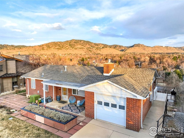 ranch-style house featuring roof with shingles, brick siding, a chimney, a garage, and a mountain view