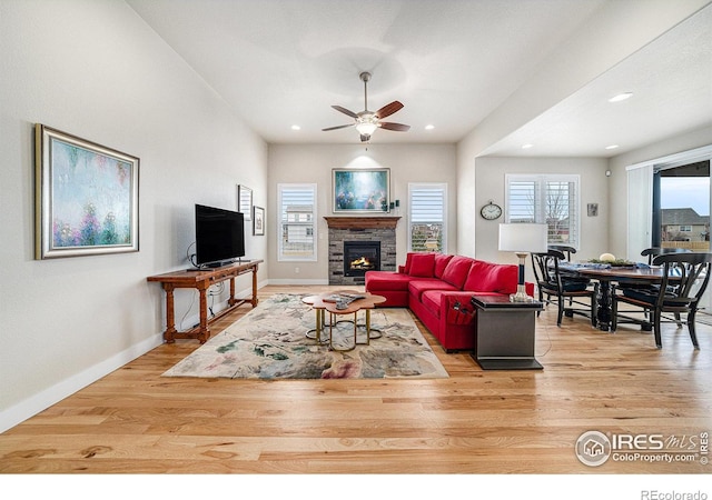 living area with baseboards, light wood-style floors, a stone fireplace, and a ceiling fan