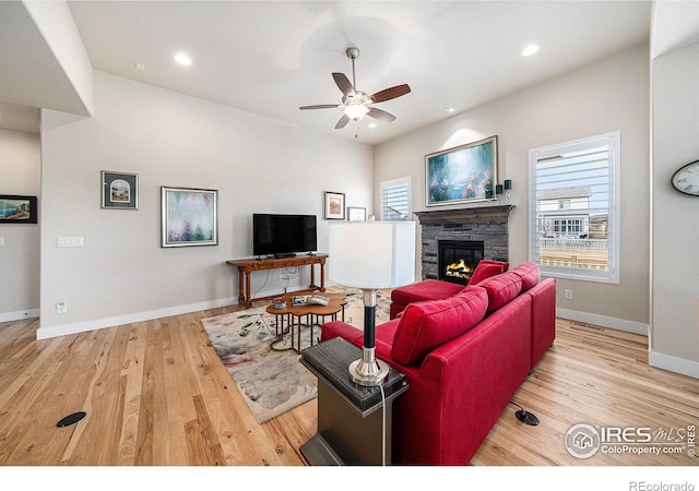 living room with a stone fireplace, plenty of natural light, wood finished floors, and ceiling fan