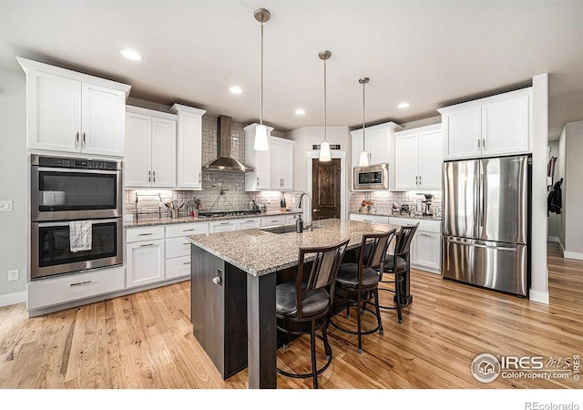 kitchen with appliances with stainless steel finishes, light wood-type flooring, wall chimney range hood, and a sink