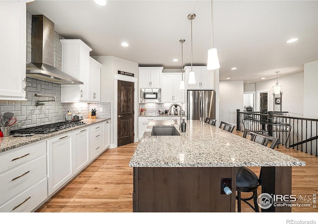 kitchen featuring a sink, stainless steel appliances, light wood-style floors, a kitchen bar, and wall chimney exhaust hood