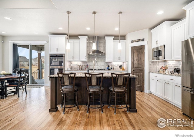 kitchen featuring a center island with sink, wall chimney exhaust hood, light wood-type flooring, and stainless steel appliances