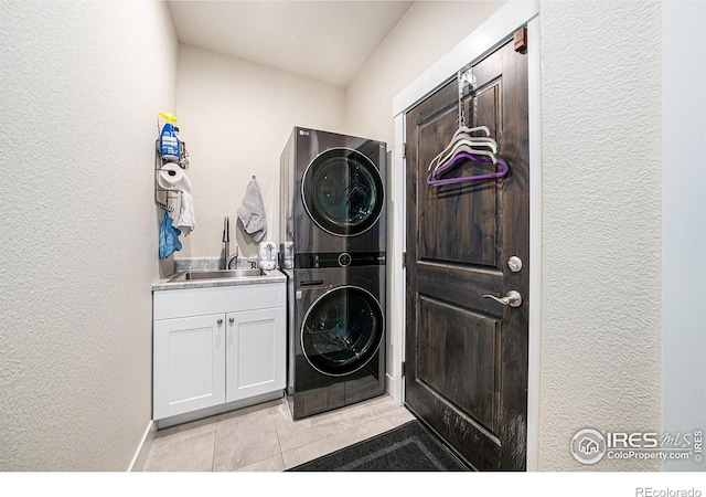 laundry room featuring light tile patterned floors, cabinet space, a sink, stacked washer and dryer, and a textured wall