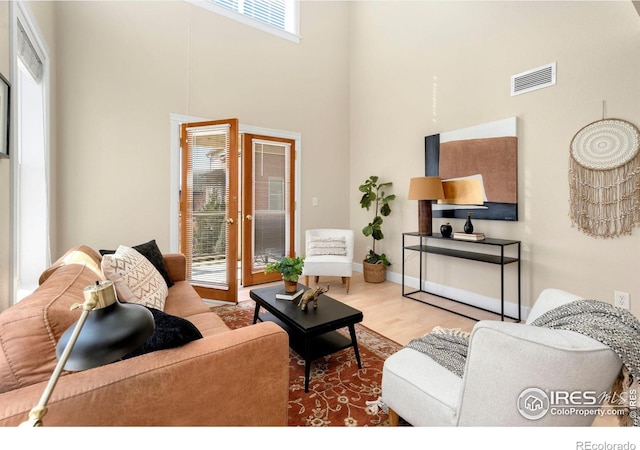 living room featuring a towering ceiling, wood finished floors, visible vents, and a wealth of natural light